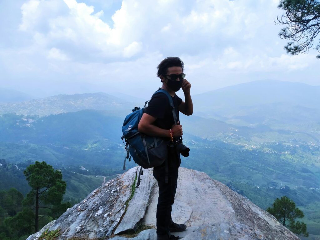 Adventurer with backpack and camera on a mountainous overlook in India.